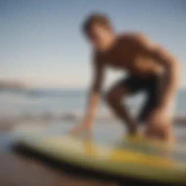 A surfer applying wax to a surfboard in a coastal setting